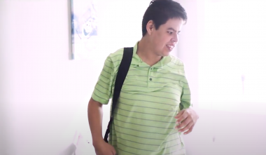 Young male with a disability wearing a striped green polo shirt and a backpack.