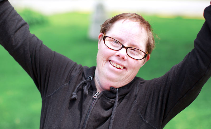 Smiling female with a disability holding her hands up in the air.
