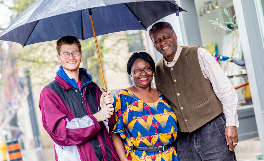 Host family of three adults in rain with umbrella
