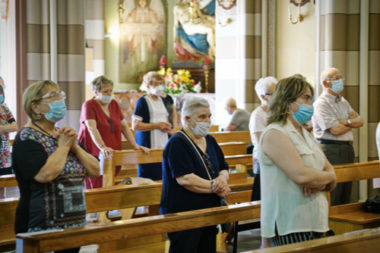 People wearing blue non medical masks while standing with distance between one another in a church.