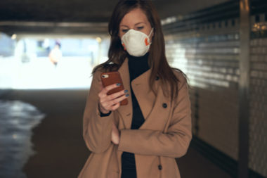 Woman wearing a blue non medical mask while looking at her cellphone.