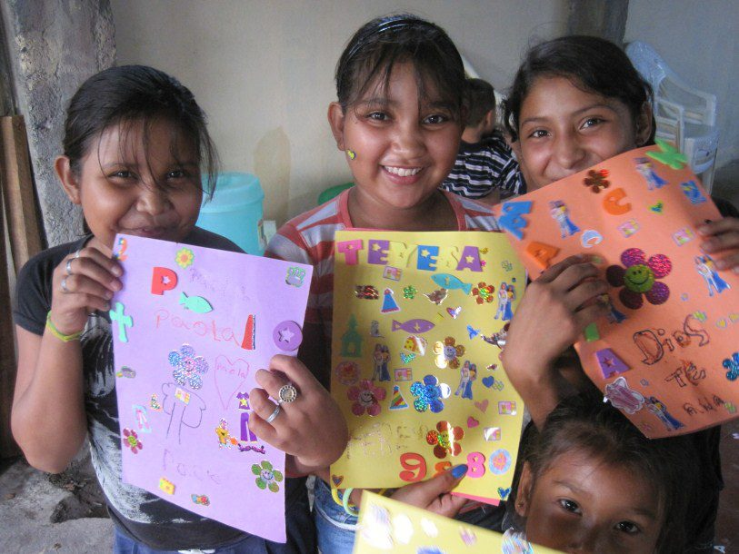 Three young girls holding up pictures of their handmade art.