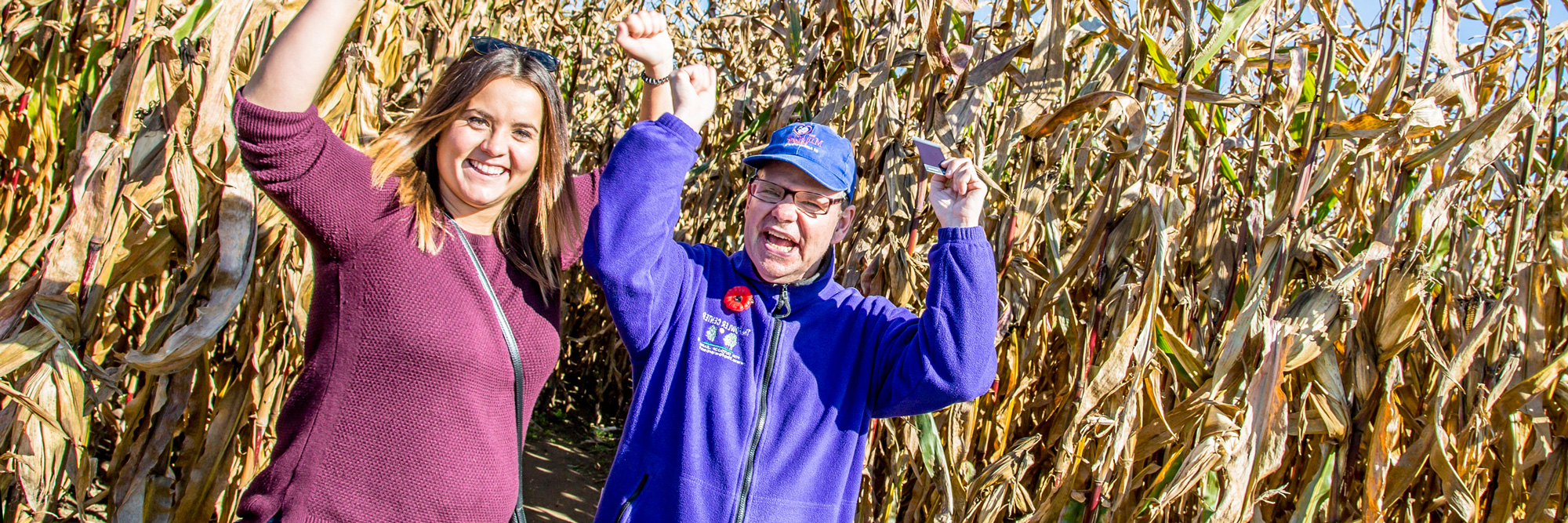 A man and a woman standing in a cornfield with hands raised in celebration