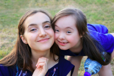 Smiling young girl with disability standing beside her sister.