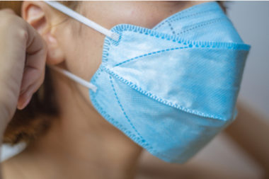 Close up image of a person wearing a blue non medical mask.